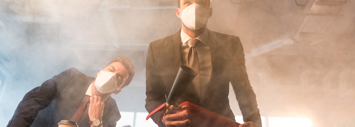Zakenman met een masker houdt een brandblusser vast in een kantoor waar brand en rook is